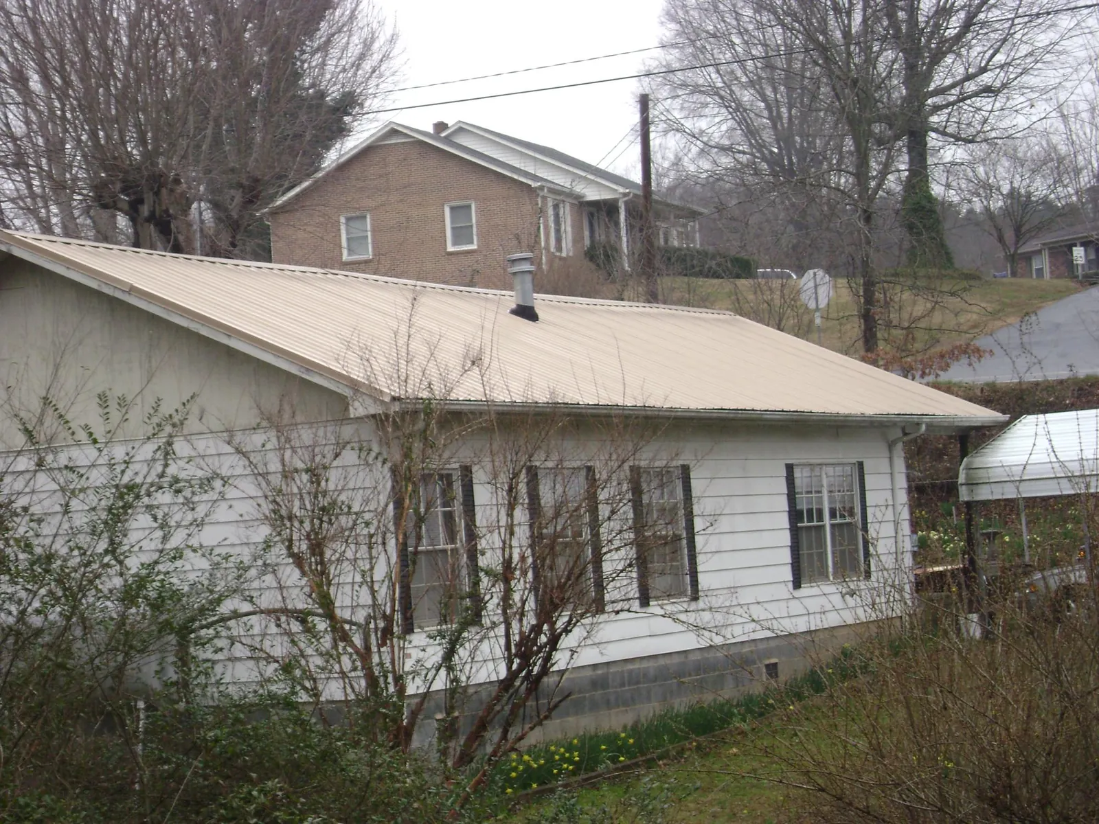 Tan metal roof on a white sided house set into a hillside — Commercial Roofing by Roofing Brothers in Doylestown